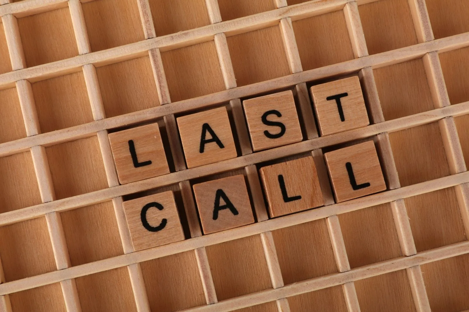 Wooden Scrabble tiles spelling 'Last Call' on a wooden grid background.